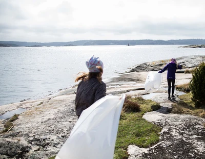 Två flickor springer med skräpplockarpåsar vid Bohuskusten.
