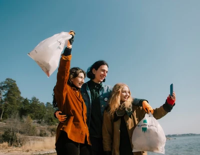 Tre glada personer på en strand med skräppåsar i händerna.