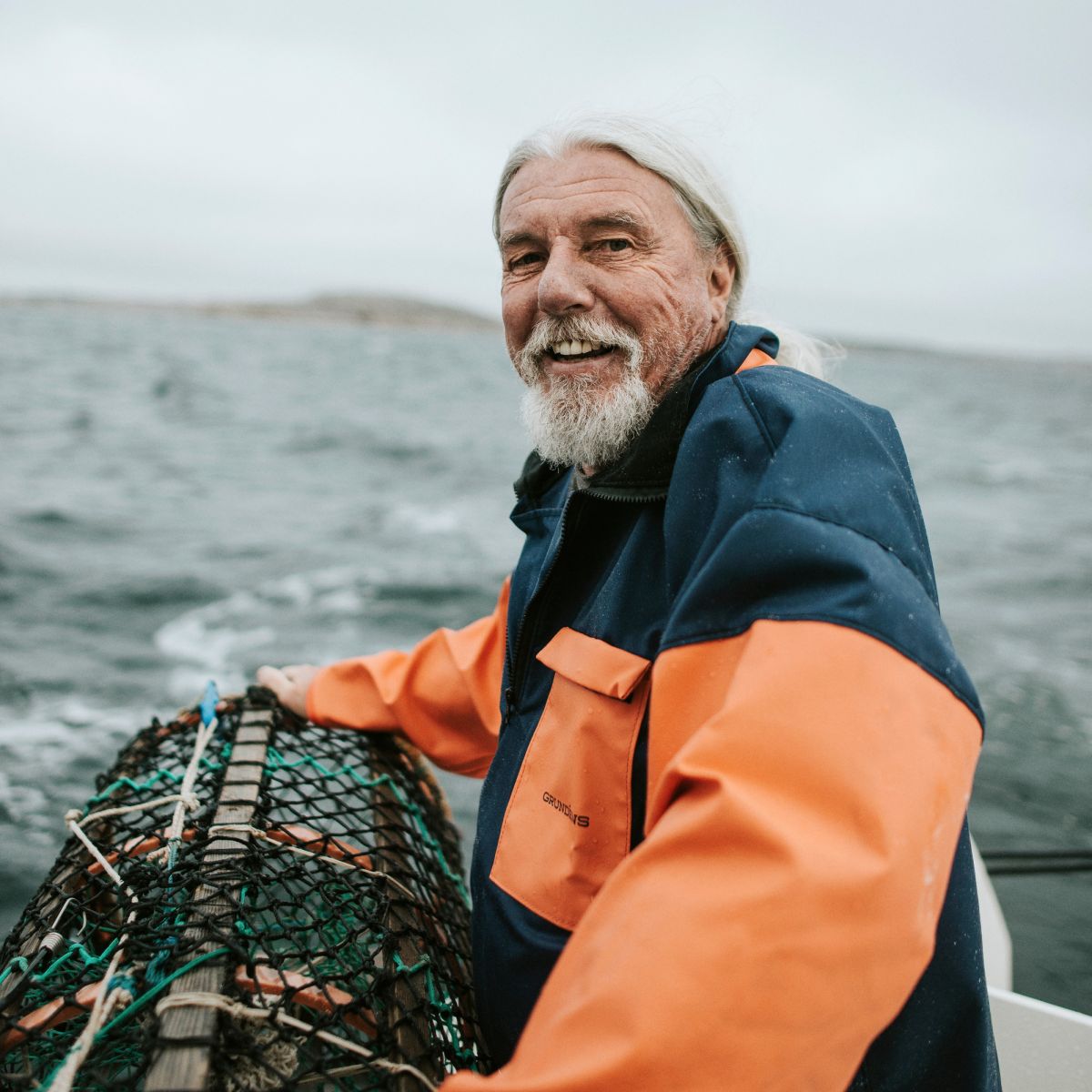 En fiskare står i sin båt och håller i en hummertina