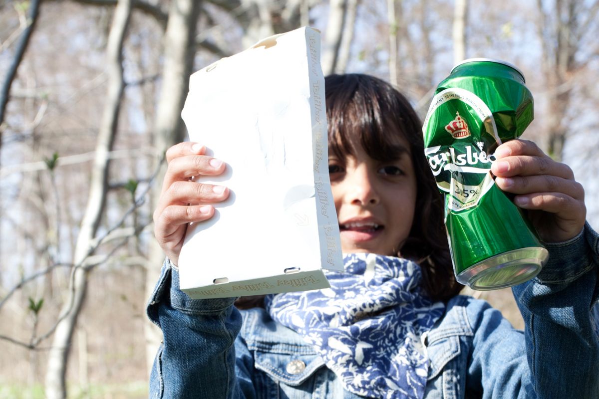 Flicka som håller två skräp - en burk och en pappersförpackning