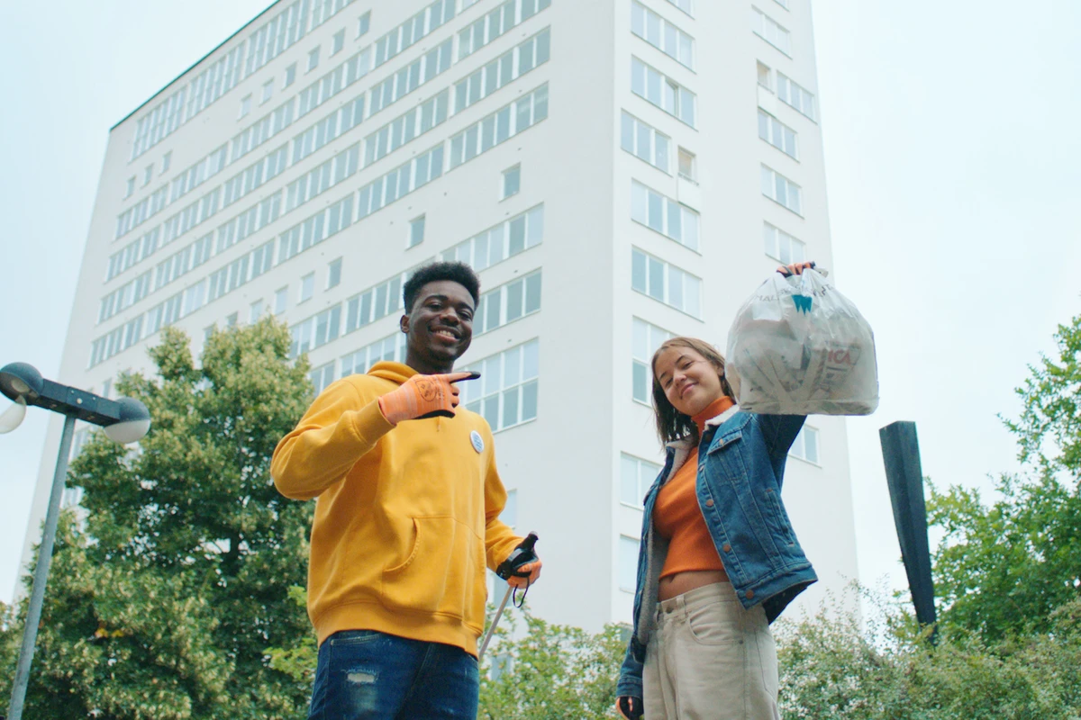 Två ungdomar i stadsmiljö håller i skräppåsar