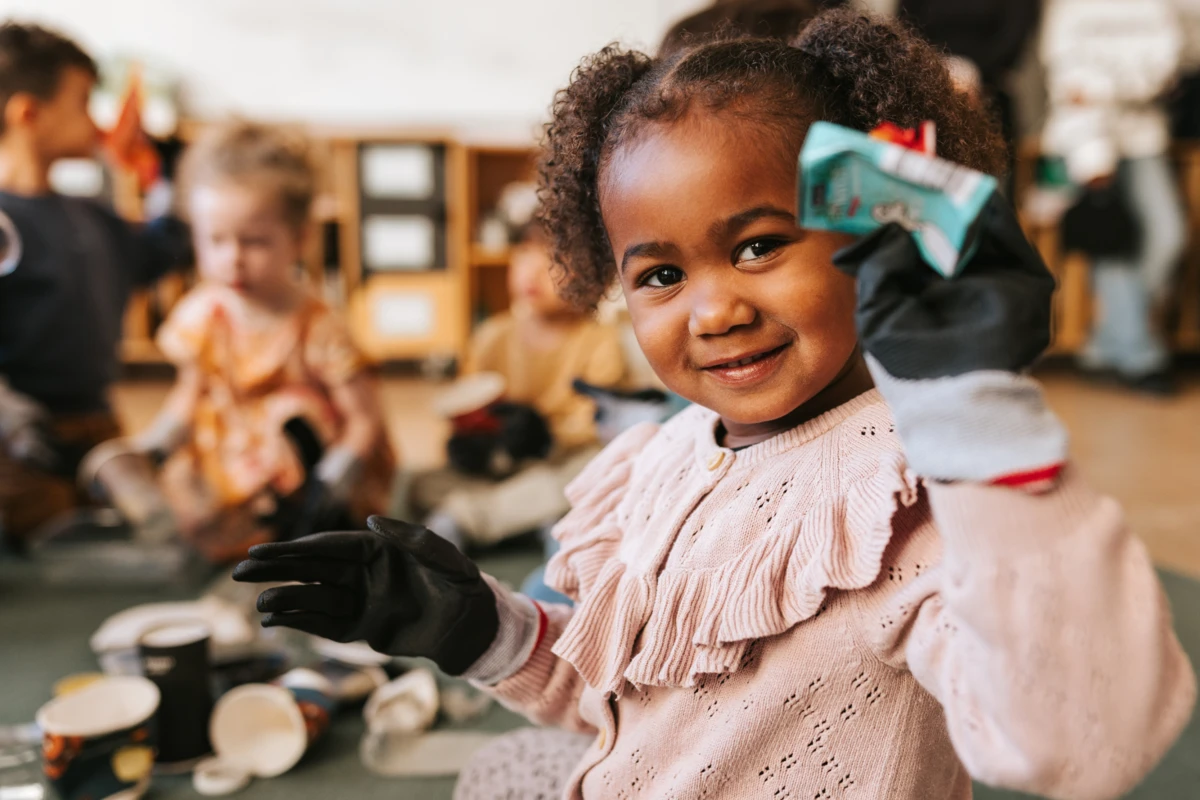 Flicka ler och håller fram skräp