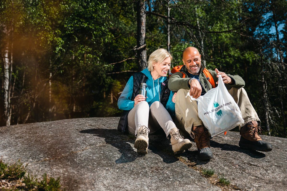 Kvinna och man sitter på berg med Håll Sverige Rent-påse