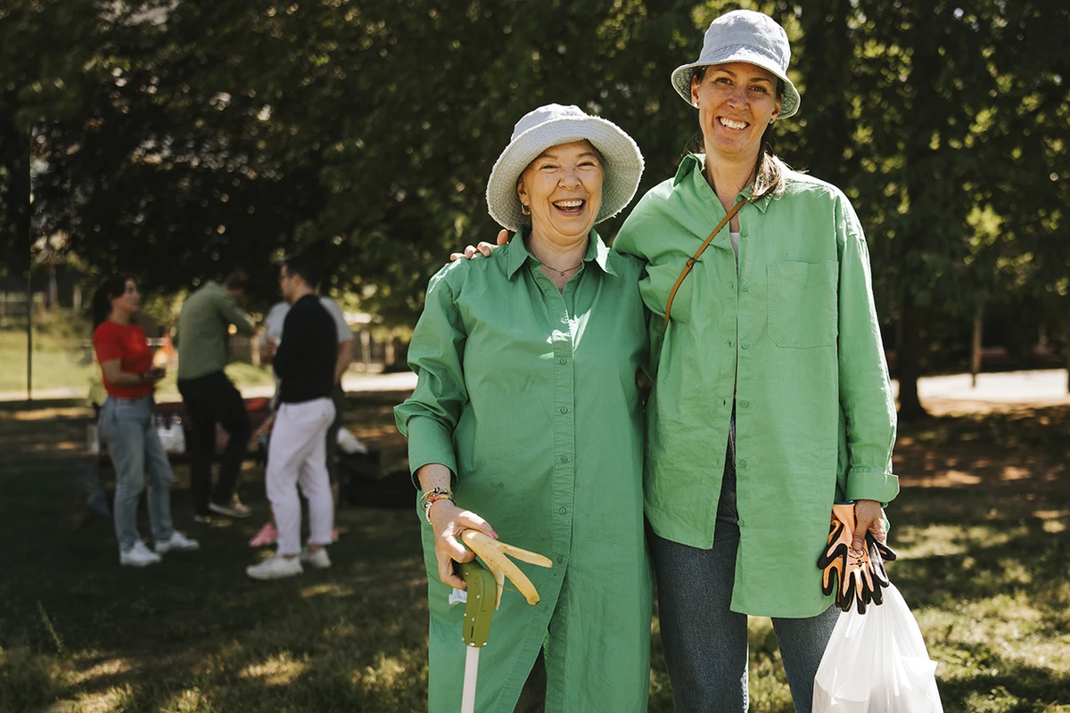 Två kvinnor utomhus som plockar skräp och ser in i kameran