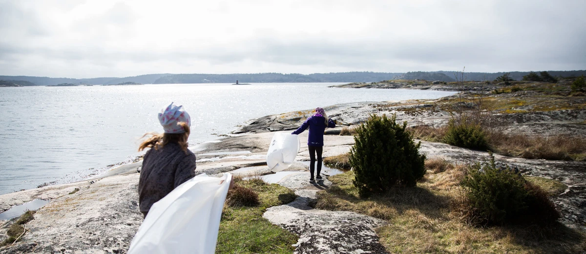 Två flickor springer med skräpplockarpåsar vid Bohuskusten.