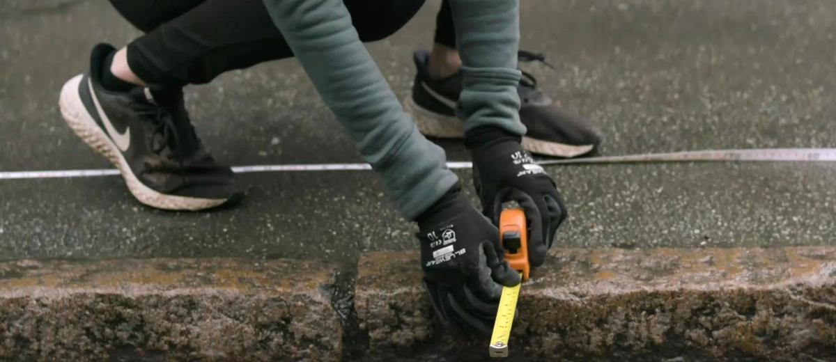 En person mäter avstånd från trottoarkant för att genomföra en skräpmätning