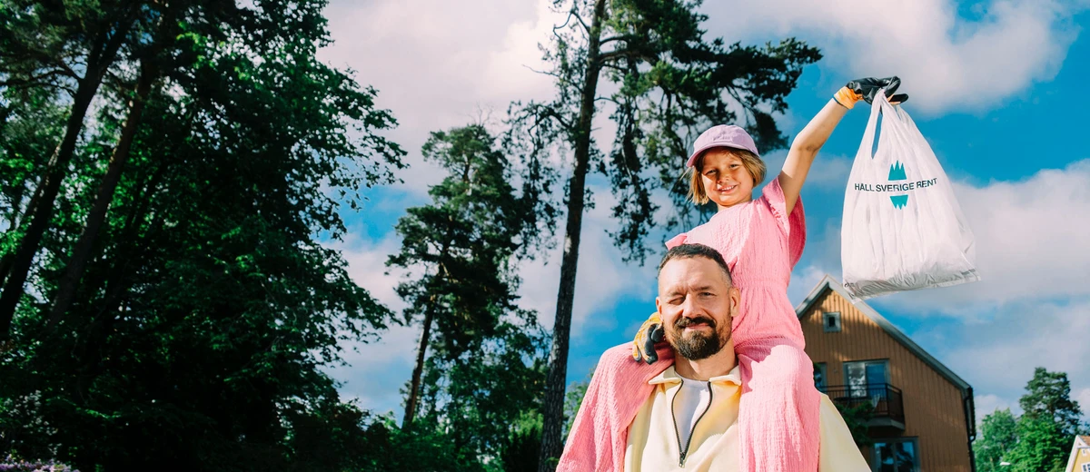 Glad flicka med skräpplockarpåse sitter på sin pappas axlar.