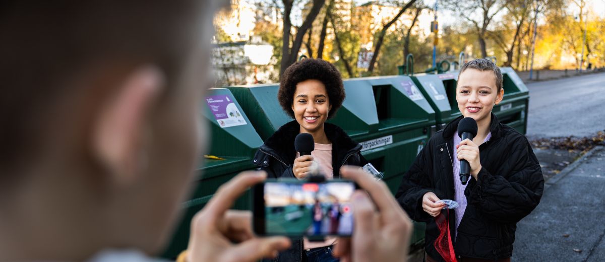 Två unga reportrar blir filmade vid en återvinningsstation