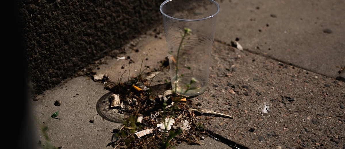 Några fimpar och en engångsmugg i plast ligger på marken