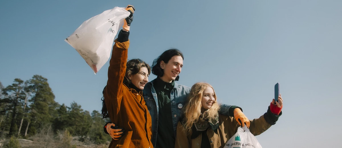 Tre glada personer som står på en strand med skräppåsar i händerna.