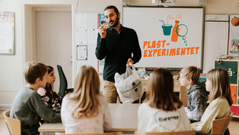 Lärare håller upp skräp med Plastexperimentets logga på whiteboard. Foto: Emma Grann