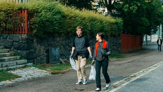 Två personer går på en trottoar och plockar skräp