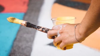 Hand som håller i en pensel och mugg med färg. Foto: Jaunt and Joy/Unsplash 