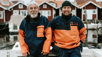 Två män står framför några fiskebodar