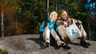 Kvinna och man sitter på berg med Håll Sverige Rent-påse