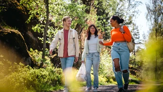 Vänner på promenad i skogen med en skräpplockarpåse