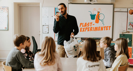 Lärare håller upp skräp med Plastexperimentets logga på whiteboard. Foto: Emma Grann