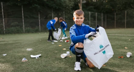 Pojke i fotbollskläder tittar in i kameran medan han plockar skräp