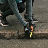 En person mäter avstånd från trottoarkant för att genomföra en skräpmätning