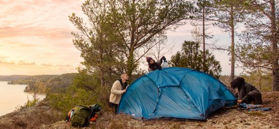 Tre personer sätter upp ett tält i naturen
